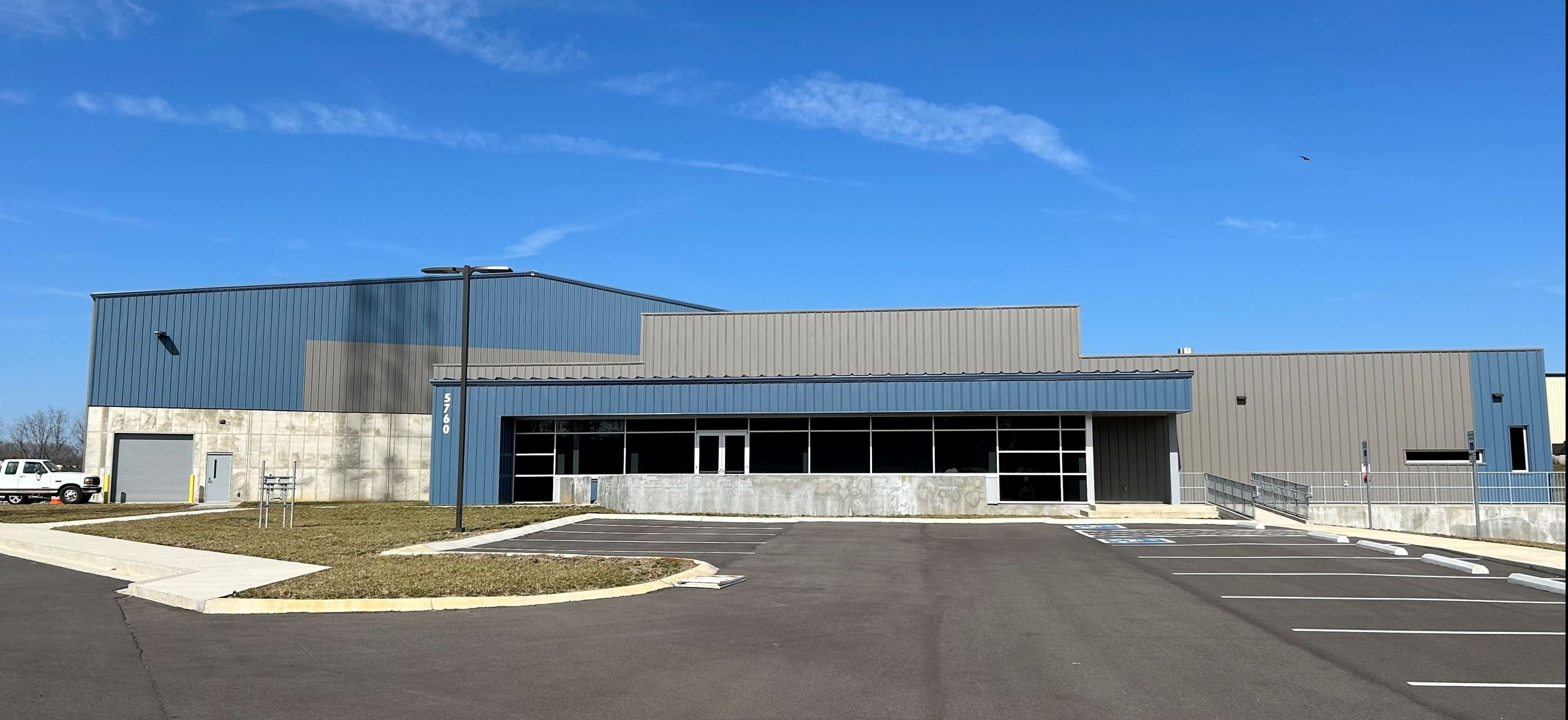 A large blue and gray warehouse with a front parking lot on a sunny day.
